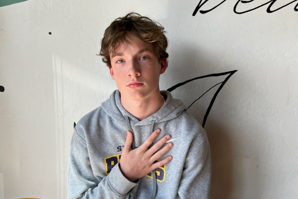 A person in a gray hoodie sitting against a wall with partial text, "life is bea," visible in the background.